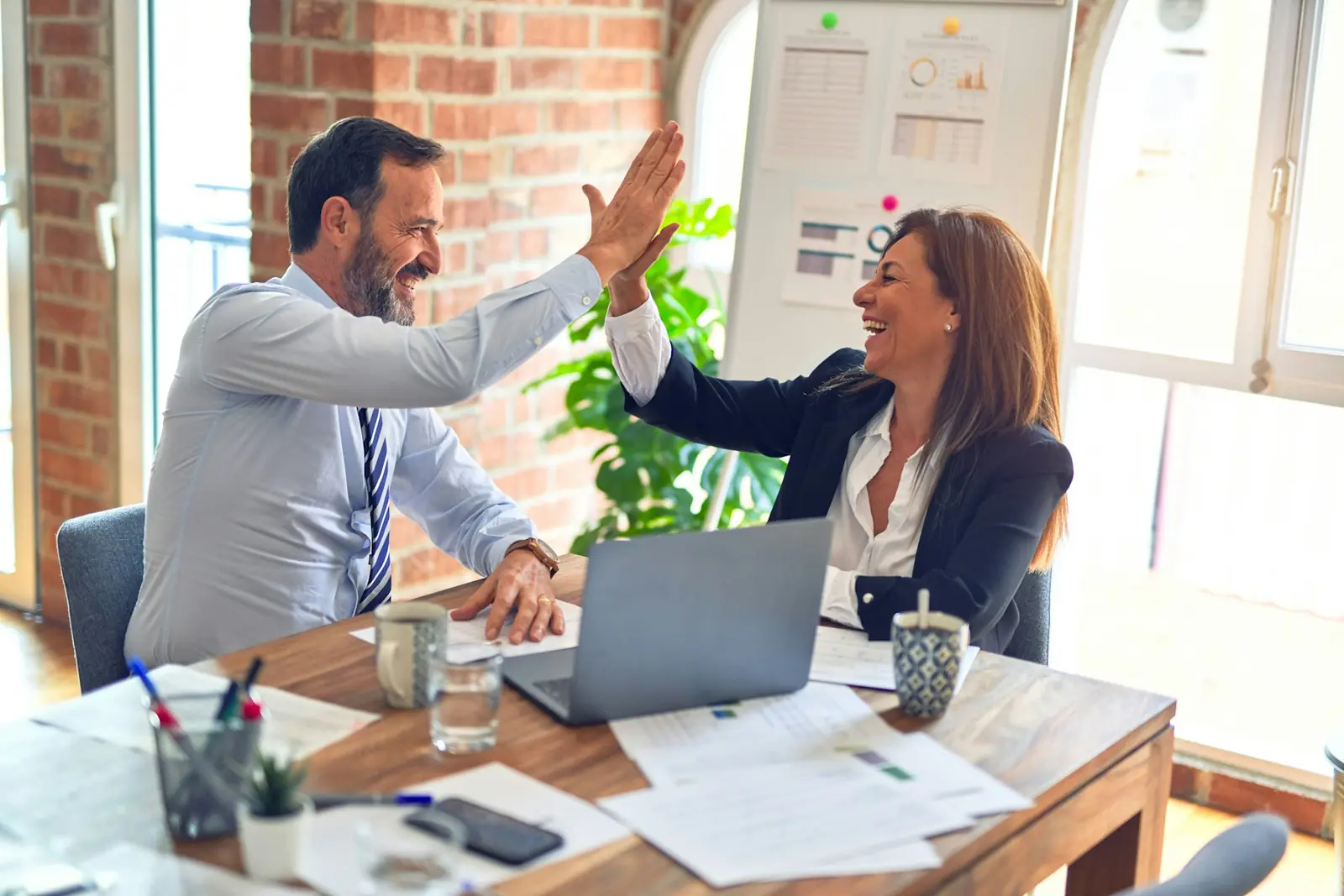 Two colleagues celebrating at a desk in a bright office
